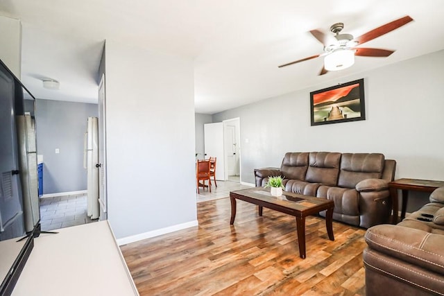 living area with baseboards, ceiling fan, and light wood finished floors