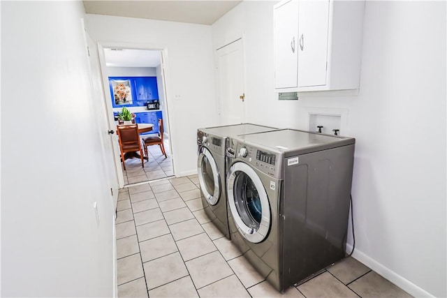 laundry room featuring washing machine and dryer, cabinet space, baseboards, and light tile patterned flooring