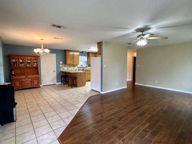 unfurnished living room featuring ceiling fan with notable chandelier and light wood-type flooring