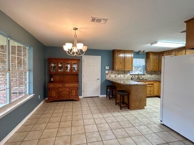 kitchen with backsplash, a kitchen breakfast bar, white refrigerator, decorative light fixtures, and kitchen peninsula