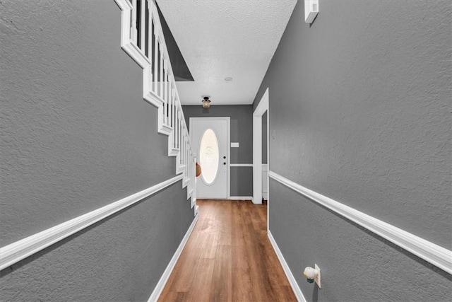 hall with a textured ceiling, wood finished floors, baseboards, stairs, and a textured wall