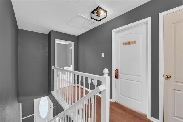 hallway with wood finished floors, attic access, an upstairs landing, and a textured ceiling