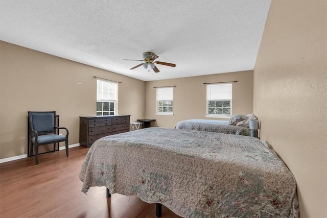 bedroom featuring a ceiling fan, wood finished floors, baseboards, and a textured ceiling