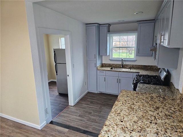 kitchen with black gas range, dark wood-style flooring, freestanding refrigerator, gray cabinets, and a sink