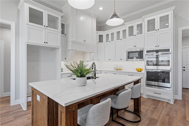 kitchen featuring light stone countertops, stainless steel appliances, white cabinetry, and an island with sink