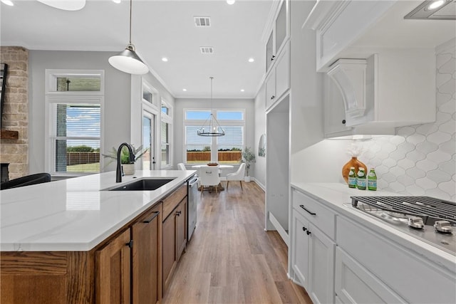 kitchen featuring sink, light hardwood / wood-style flooring, backsplash, a fireplace, and white cabinets