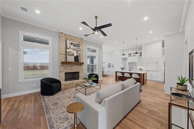 living room featuring ornamental molding, ceiling fan, sink, light hardwood / wood-style flooring, and a stone fireplace