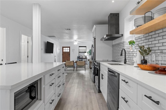 kitchen featuring open shelves, wall chimney range hood, light countertops, appliances with stainless steel finishes, and a sink