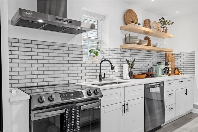 kitchen with a sink, open shelves, stainless steel appliances, wall chimney exhaust hood, and white cabinets