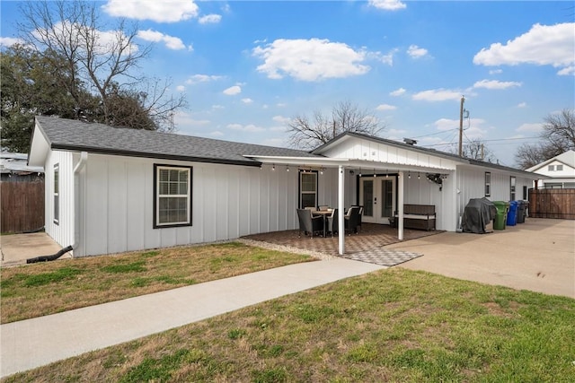 view of front of house with board and batten siding, fence, a front yard, french doors, and a patio area