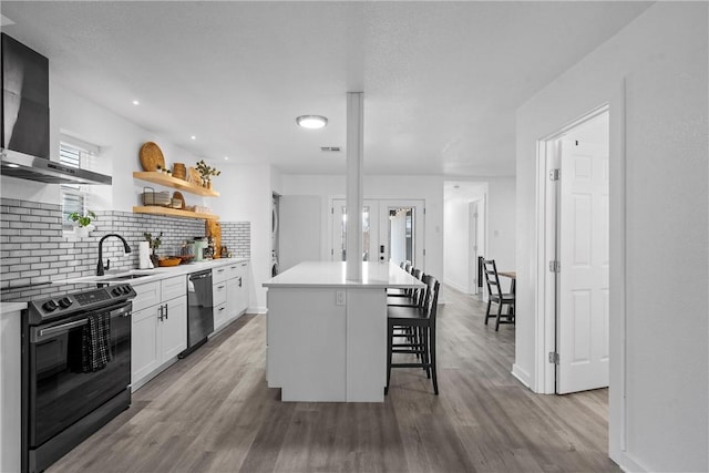 kitchen featuring black range with electric cooktop, dishwashing machine, a kitchen breakfast bar, wall chimney exhaust hood, and a sink