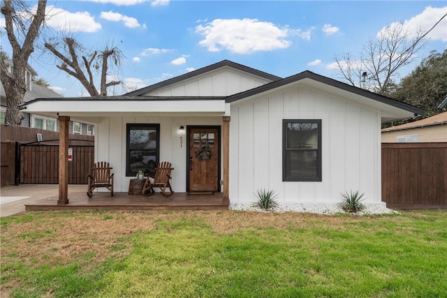 view of front of property featuring a front yard, covered porch, fence, and board and batten siding