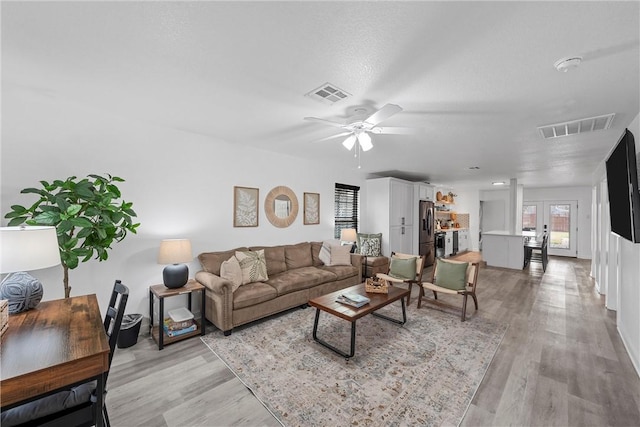 living room with light wood-type flooring, visible vents, and french doors