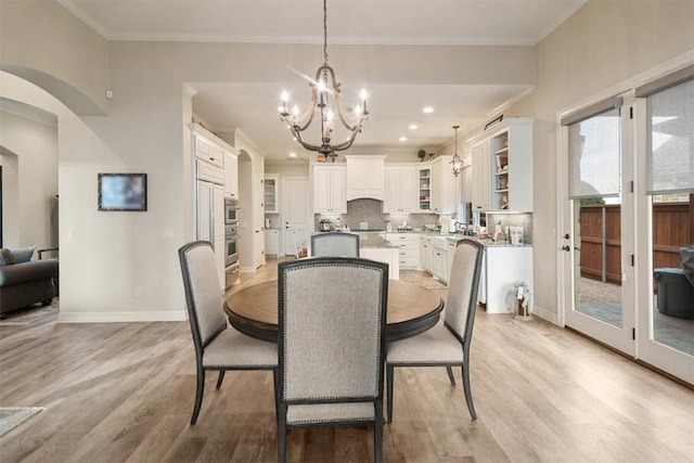 dining area with light hardwood / wood-style floors, ornamental molding, and an inviting chandelier