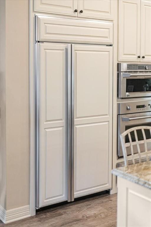 interior space featuring stainless steel double oven, light hardwood / wood-style flooring, light stone counters, and white cabinetry