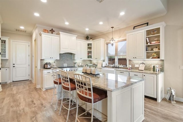 kitchen with white cabinets, a kitchen island, hanging light fixtures, and light hardwood / wood-style floors