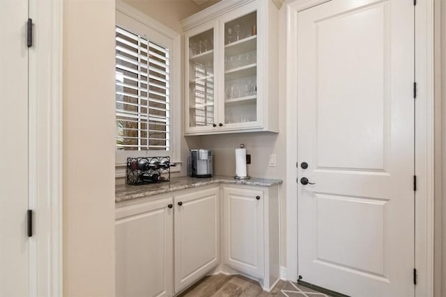 bar with light stone counters, light hardwood / wood-style flooring, and white cabinets