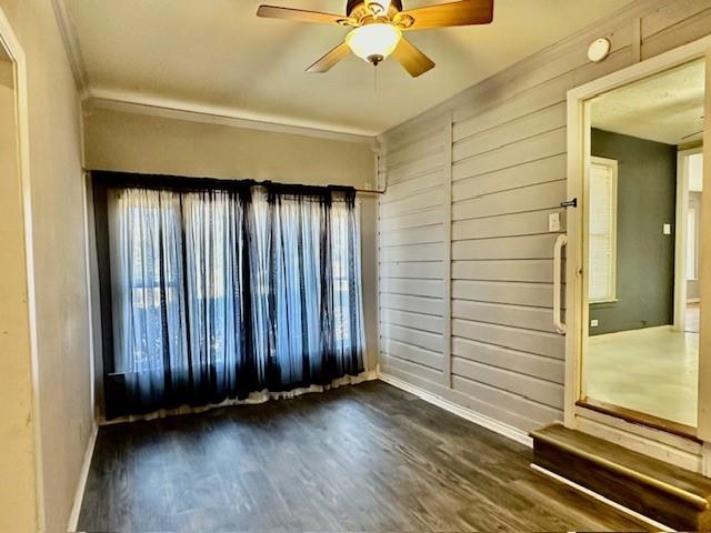 spare room featuring wood walls, dark hardwood / wood-style floors, ceiling fan, and crown molding