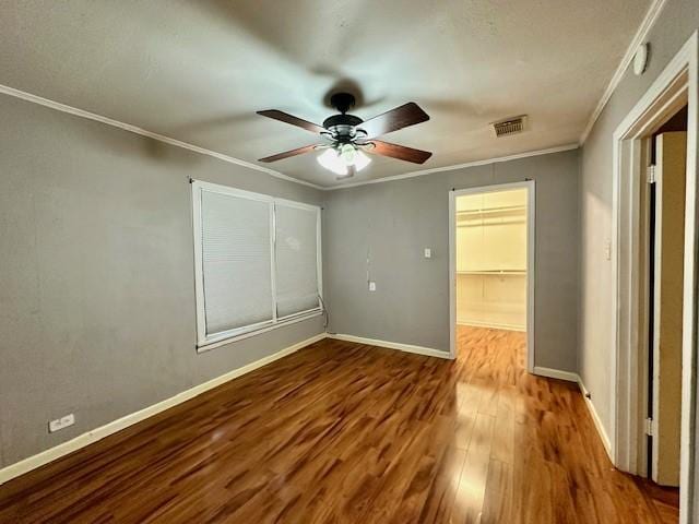 unfurnished bedroom featuring ceiling fan, crown molding, wood-type flooring, a walk in closet, and a closet