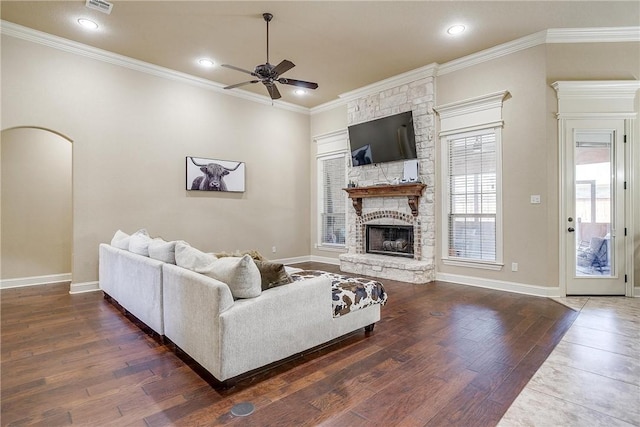 living room featuring a stone fireplace, ceiling fan, dark hardwood / wood-style floors, and ornamental molding