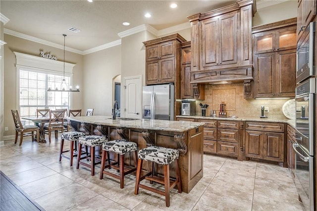 kitchen featuring appliances with stainless steel finishes, ornamental molding, custom range hood, a kitchen island with sink, and decorative light fixtures