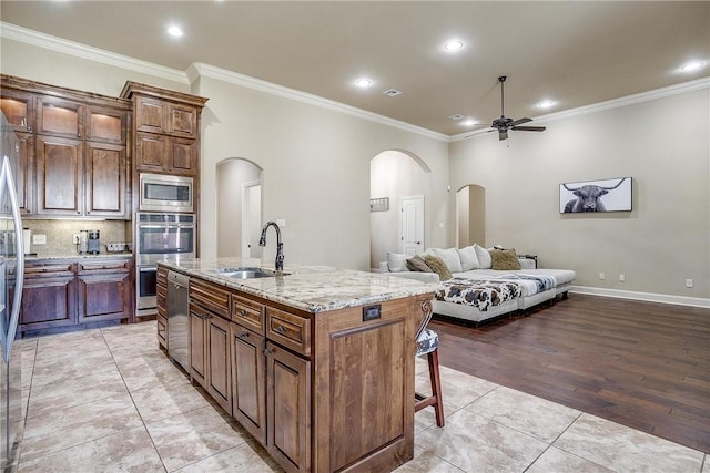 kitchen with sink, stainless steel appliances, crown molding, a kitchen island with sink, and light wood-type flooring