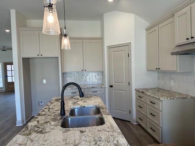 kitchen featuring a sink, under cabinet range hood, dark wood-style floors, light stone countertops, and hanging light fixtures