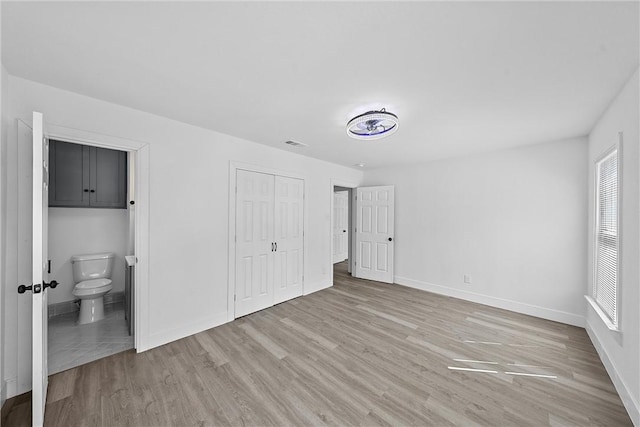 unfurnished bedroom featuring light hardwood / wood-style floors, a closet, and ensuite bath