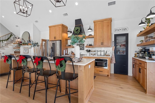 kitchen featuring a kitchen breakfast bar, stainless steel appliances, vaulted ceiling, light hardwood / wood-style floors, and a kitchen island