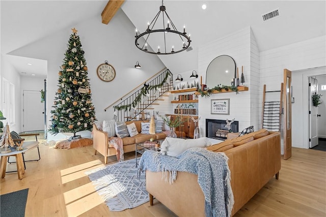 living room featuring beam ceiling, a large fireplace, high vaulted ceiling, a chandelier, and light hardwood / wood-style floors