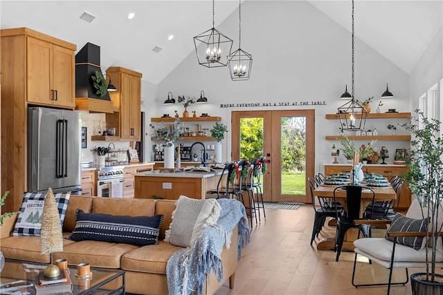 kitchen featuring appliances with stainless steel finishes, custom exhaust hood, high vaulted ceiling, light hardwood / wood-style floors, and an island with sink