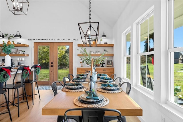 dining space with french doors, light wood-type flooring, an inviting chandelier, and lofted ceiling