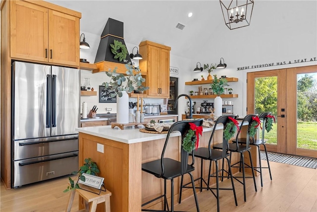 kitchen featuring french doors, a kitchen breakfast bar, a kitchen island with sink, high end fridge, and light wood-type flooring