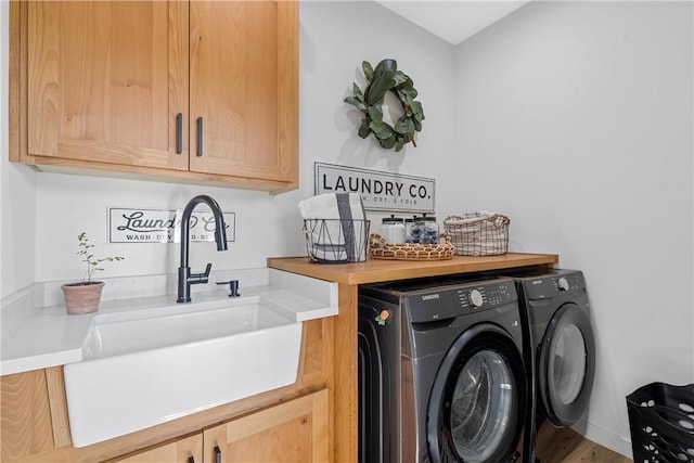 washroom featuring washing machine and clothes dryer, sink, hardwood / wood-style floors, and cabinets