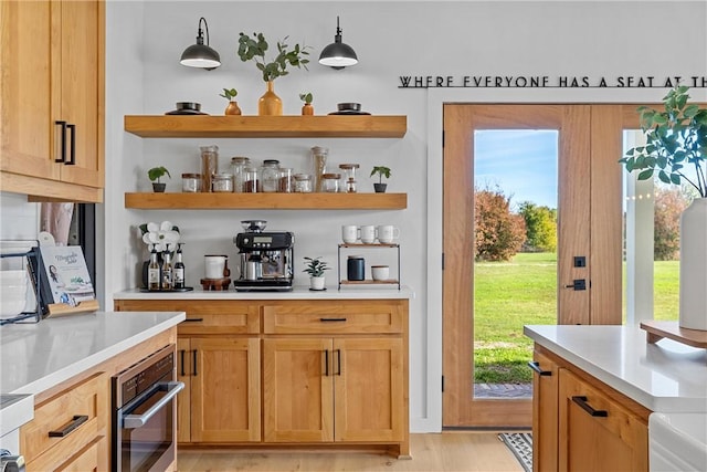 bar featuring stainless steel oven, light hardwood / wood-style floors, and hanging light fixtures