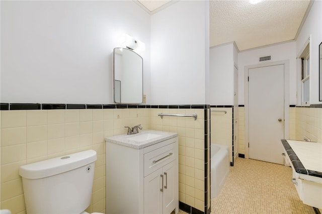 bathroom featuring vanity, a bathing tub, toilet, a textured ceiling, and tile walls