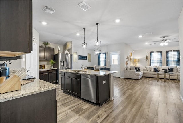 kitchen featuring pendant lighting, a kitchen island with sink, light stone countertops, appliances with stainless steel finishes, and light hardwood / wood-style floors