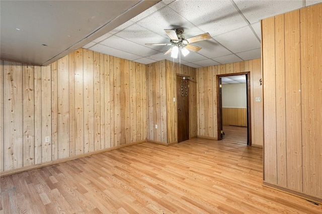 spare room featuring hardwood / wood-style flooring, a drop ceiling, wooden walls, and ceiling fan