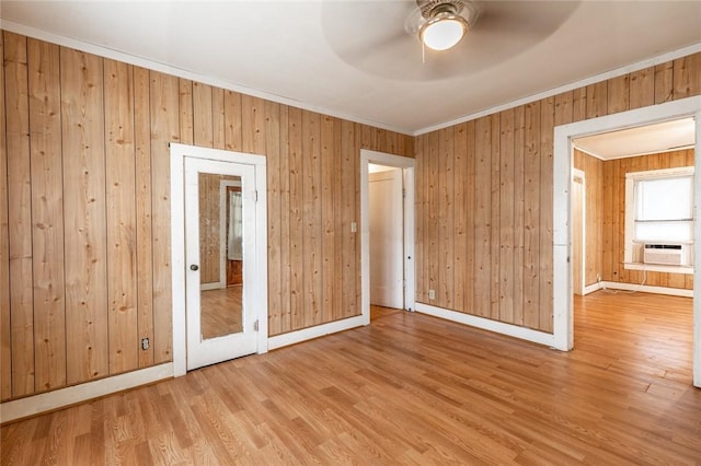 spare room featuring wooden walls, crown molding, ceiling fan, and light hardwood / wood-style floors