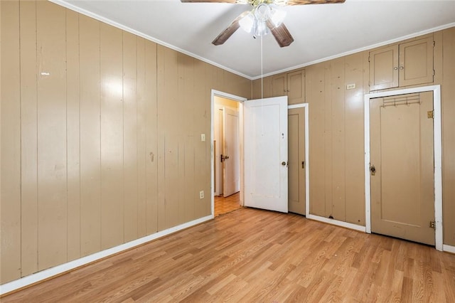 unfurnished bedroom with ceiling fan, wood walls, and light hardwood / wood-style flooring