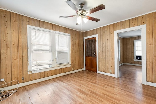 spare room featuring ceiling fan, light wood-type flooring, ornamental molding, and wooden walls