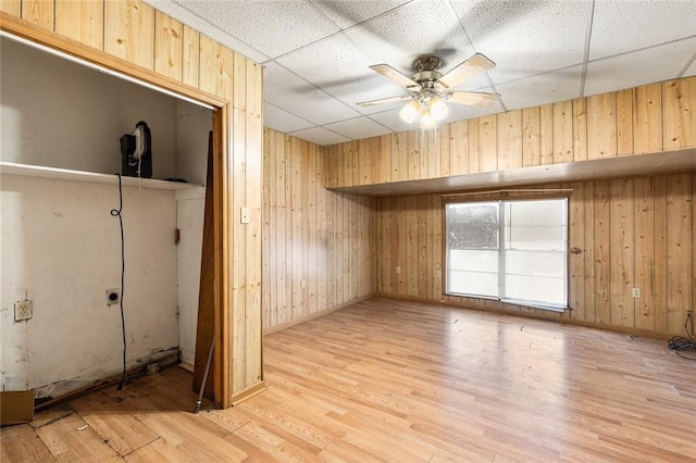 unfurnished room with hardwood / wood-style floors, a drop ceiling, wood walls, and ceiling fan