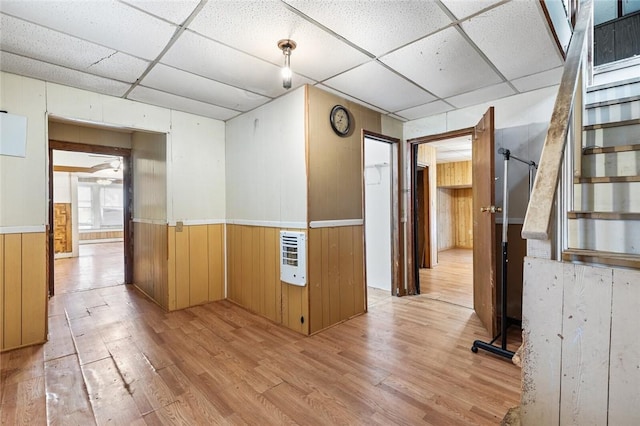 hallway featuring heating unit, light hardwood / wood-style floors, a drop ceiling, and wood walls