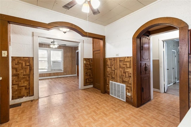 unfurnished room with ceiling fan, wooden walls, and light parquet floors