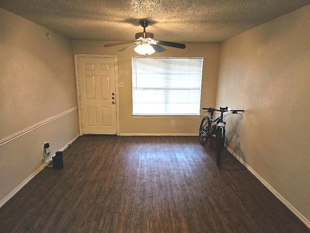 empty room with a textured ceiling, ceiling fan, and dark hardwood / wood-style floors