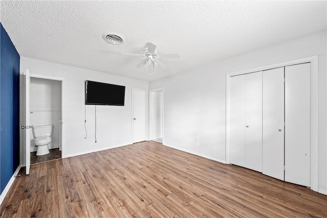 unfurnished bedroom featuring hardwood / wood-style flooring, a closet, ensuite bathroom, and a textured ceiling