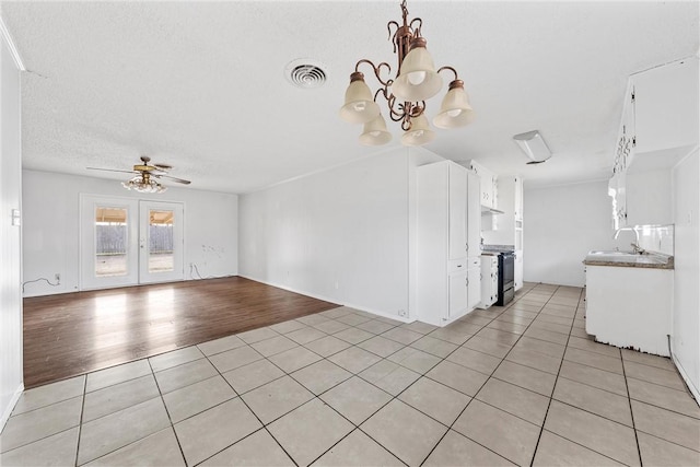 unfurnished living room featuring sink, ceiling fan with notable chandelier, a textured ceiling, and light tile patterned floors