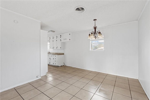 unfurnished dining area featuring sink, light tile patterned floors, ornamental molding, a textured ceiling, and a chandelier