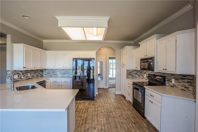 kitchen featuring kitchen peninsula, ornamental molding, sink, black appliances, and white cabinetry