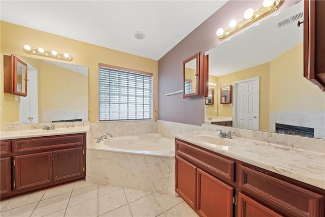 bathroom featuring a tile fireplace, vanity, tile patterned floors, and tiled tub